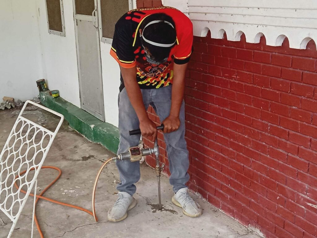sub slab soil injection Technician from Jansen Pest Control Bohol drilling into concrete outside a building, preparing for termite barrier installation